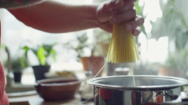 Makarna pişirirken spagettiyi kaynayan suyla birlikte tencereye koyan şefin yakın çekim görüntüleri.
