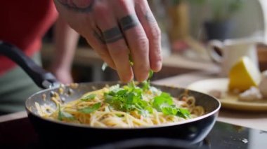 Yemek pişirirken sıcak makarnaya maydanoz yaprağı ekleyen erkek şefin yakın görüntüsü.