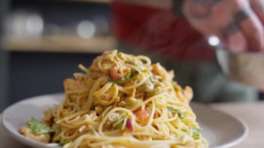 Şef 'in tabakta servis edilen yeni pişmiş makarnanın üzerine baharat serpiştirdiği yakın çekim.