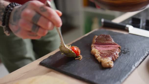 나무판에 쇠고기 스테이크 옆에서 토마토 샐러드를 제공하는 요리사의 가까이 — 비디오