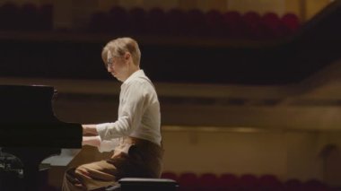 Piyanist konser salonunda resitalden önce sahnede müzik çalıyor.
