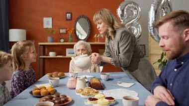 Büyükannenin doğum gününde aile üyeleri için çay dolduran bir kadın.