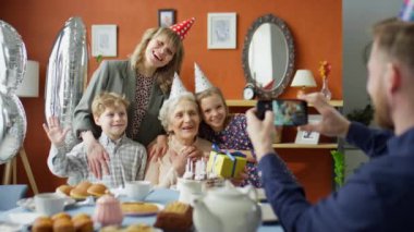 Mutlu aile ve büyükannenin akıllı telefonuyla evde doğum günü partisinde fotoğraf çeken adam.