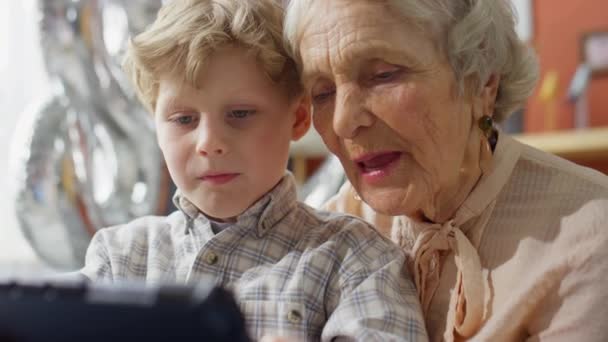 家で一緒に時間を過ごしながらデジタルタブレットで遊んでいるとき 祖母は小さな孫と話すのが大好きです — ストック動画