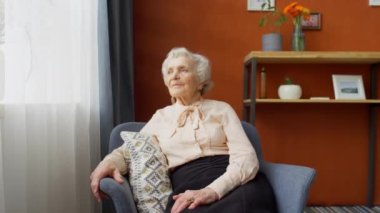 Evdeki koltukta oturan ve kameraya poz veren zarif, yaşlı bir kadının portre fotoğrafını yakınlaştır.