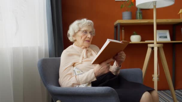 Gözlüklü Yaşlı Kadının Evdeki Koltukta Oturup Kitap Okuduğu Fotoğrafı Yakınlaştır — Stok video