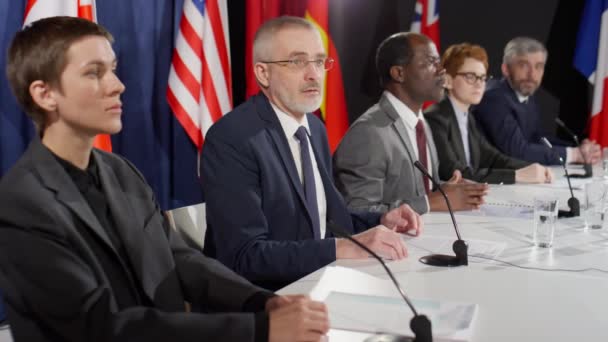 Högre Kaukasisk Politiker Som Sitter Vid Presskonferensbordet Med Multietniska Deltagare — Stockvideo