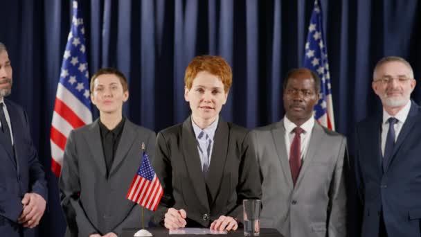 在新闻发布会上 站在讲台上高举美国国旗的女政治家们发表了成功的演讲 并在多种族同事们欢呼她时面带微笑 — 图库视频影像