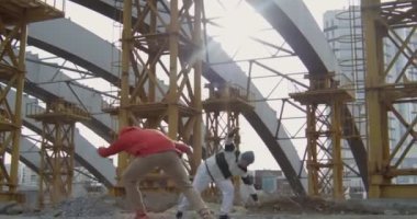 İki sporcu çocuk şehirde inşaat alanında park ederken ağır çekimde destansı yan taklalar atıyor.