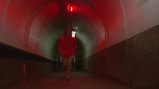 赤い光で都市トンネルを通ってカメラに向かって走っている若いパルクール選手のドリーショットとフロントフリップを行う — ストック動画