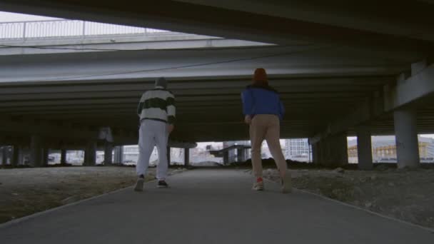 都市部の橋の下を走る2人のプロの駐車場の遅い動きのショットの後と一緒にサイドフリップを実行 — ストック動画