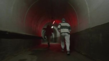 İki parkur sporcusunun kırmızı ışıkta karanlık tünelde koşup serbest koşma alıştırması yaparken yan taklalar atması.