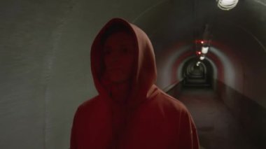 Kapüşonlu genç akşam üstü yanıp sönen kırmızı ışıkla karanlık tünelde yürüyor.