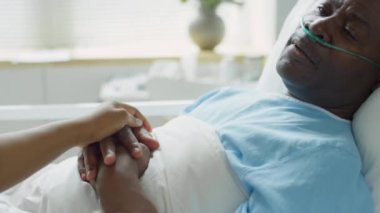 Burun kanülü hasta Afro-Amerikan bir adamın, hastane yatağında uzanmış, sevgi dolu eşiyle elini tutarken görüntüsünü kaldır.
