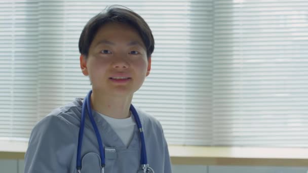 診療所勤務中にカメラを見て笑顔で正のアジア系女性医師の胸を追跡 — ストック動画