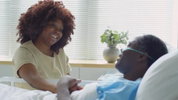 Позитивна Афро Американська Жінка Сидить Біля Ліжка Лікарні Тримаючи Руку — стокове відео