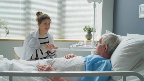 病院病棟のベッドに座っている研究室のコートの女性のショットでズーム 病気の祖父に耳を傾け 治療中にサポートしながら 彼の手を保持 — ストック動画