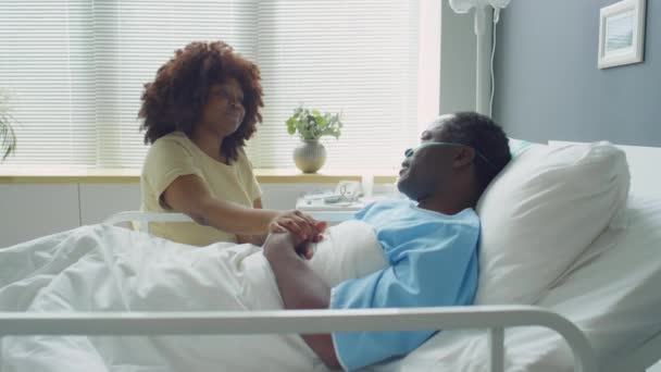 在医院病房的病床边 手牵着生病丈夫的手 在探访他时与他交谈时 放大了对爱的非洲裔美国妻子的拍照 — 图库视频影像