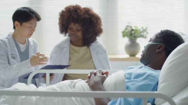 非洲裔美国人在医院病房卧床时鼻腔拉张躺在床上 与妻子和亚洲女医生讨论治疗方案 — 图库视频影像