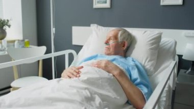 Geniz kanülü hasta yaşlı adamın hastane koğuşundaki yatağında yatıp pencereden bakarken görüntüsünü yakınlaştır.