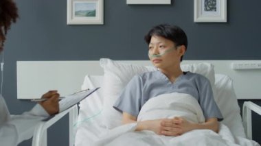 Afro-Amerikalı doktor hastane koğuşunda yatıp Asyalı kadın hastalara tedavi planlarını anlatıyor.