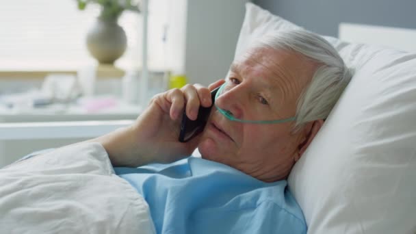 病院病棟のベッドの上に寝そべって携帯電話で話す鼻カヌラと病気の高齢者 — ストック動画