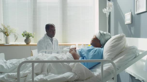 若い女性患者の手を保持し 病院で治療中にサポートしながら彼女と話すアフリカ系アメリカ人医師のショットでズーム — ストック動画
