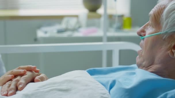 年老体衰的考卡辛男子 头戴鼻涕 躺在病床上 一边和年轻的亚洲护士说话 一边摸着他的手支撑着他 — 图库视频影像