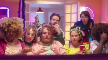Bir grup modaya uygun giyinmiş çok ırklı arkadaşlar TV 'de spor müsabakalarını izliyor ve en sevilen takımın zaferini neon ışıkla kutlarken heyecanla bağırıyorlar.
