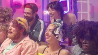 Moda kıyafetleri içinde üniversite arkadaşlarıyla kanepede oturup, içki içip, televizyon izleyip, neon ışıklı ev partileri yaparken kahkahalar atıyorlar.
