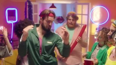 Yeşil eşofman ve fitness saç bandı takmış genç sakallı adamı, 90 'ların temalı partisinde arkadaşlarıyla dans ederken çek. Disko ışıkları ve neon süslemelerle.