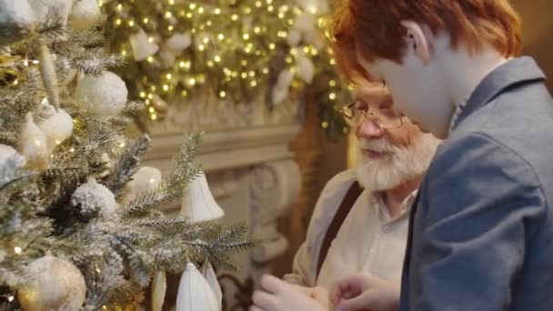 Kleine Jongen Versieren Kerstboom Thuis Dan Knuffelen Gelukkige Grootvader Tijdens — Stockvideo