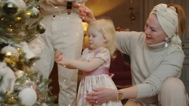 Schattig Klein Meisje Senior Grootouders Versieren Kerstboom Met Bloemenslinger Tijdens — Stockvideo