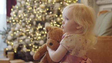 Sevimli küçük kız elinde ayı oyuncağı ve Noel arifesinde evde oynarken etrafında dönüyor.