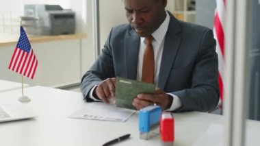 Afro-Amerikan vize memuru ABD büyükelçiliğinde iş günü pasaport ve başvuru formlarını kontrol ediyor