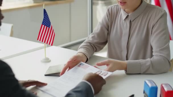 若い白人女性がアフリカ系アメリカ人のビザ担当者に書類を渡し 米国大使館でのインタビュー中に彼と話す — ストック動画