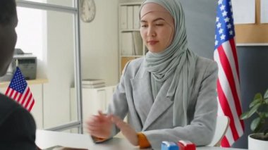 ABD büyükelçiliğinde yürüyen tesettürlü genç Müslüman kadın, Afrikalı Amerikan konsolosluğuna belgeler veriyor ve vizeye başvururken sorularını cevaplıyor.