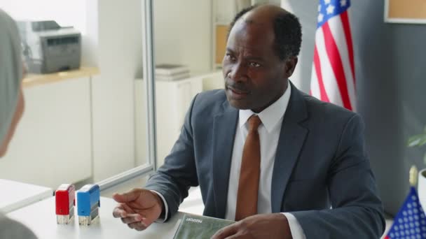 アフリカ系アメリカ人のビザ担当官は 米国大使館でのインタビュー後 申請書に承認されたスタンプを押し ヒジャーブ州のイスラム教徒女性に文書を与える — ストック動画