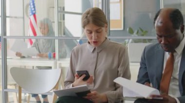 Telefon kullanan genç beyaz bir kadın ve resmi takım elbiseli Afrikalı Amerikalı bir adama ABD elçiliğinde görüşme sırasında vize başvuru formu doldurması için yardım ediyor.
