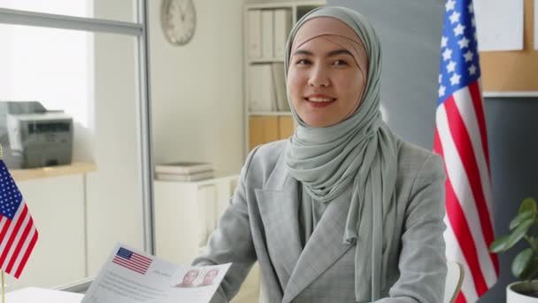在签证面试中 穿着头巾坐在美国大使馆里 微笑着摆出一副相机的年轻穆斯林女子的画像 — 图库视频影像