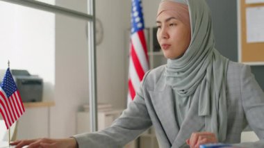 Genç müslüman kadının başörtüsü altında dizüstü bilgisayar kullanırken ve pasaport kontrol ederken ABD büyükelçiliğinde vize memuru olarak çalışırken.