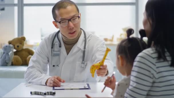Asijský Pediatr Bílém Plášti Brýle Dávat Žirafa Hračka Roztomilé Holčičce — Stock video