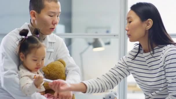 아시아 의사는 병원에서 진찰을 손전등을 가지고 장난감을 가지고 어린아이와 어머니와 — 비디오