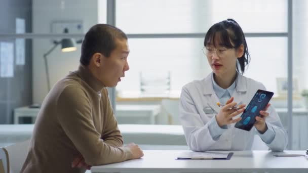 診療所で診察を受けながら男性患者にデジタルタブレットでX線画像を説明するアジア女性医師 — ストック動画