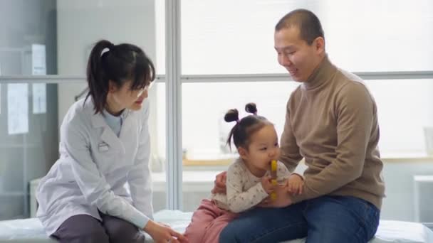 亚洲父亲坐在诊所的医疗沙发上 与顽皮的幼儿女儿坐在一起 与女儿科医生进行咨询 — 图库视频影像
