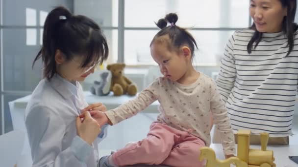 アジアの幼児女の子プレイとともにバッジの女性小児科医しばらく訪問クリニックとともに母のために定期的なチェック — ストック動画