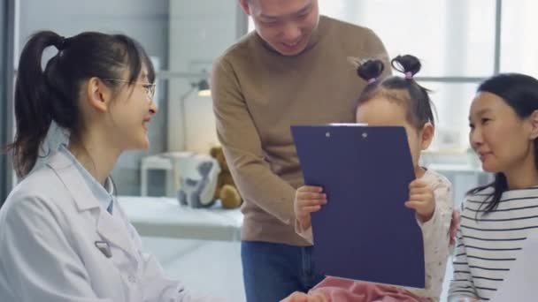 亚洲女儿科医生在探访诊所的过程中 与作为幼儿女儿的父母交谈 玩弄病史 — 图库视频影像