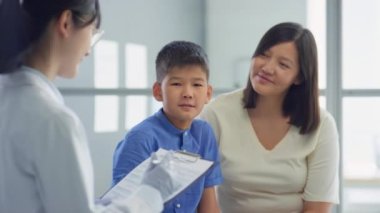Asyalı ergen çocuk ve annesi, klinikteki danışmanlık sırasında not alırken kadın doktorla konuşuyor.