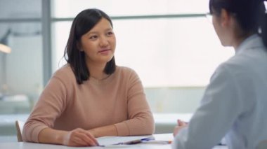 Asyalı kadın klinikte oturuyor ve muayene sırasında kadın doktorla konuşuyor.