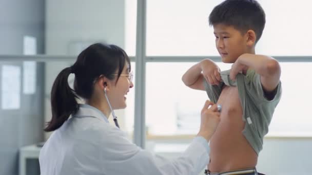 아시아 의사가 청진기를 가지고 소년을 진찰하고 검진을 동안그와 이야기를 나누다 — 비디오